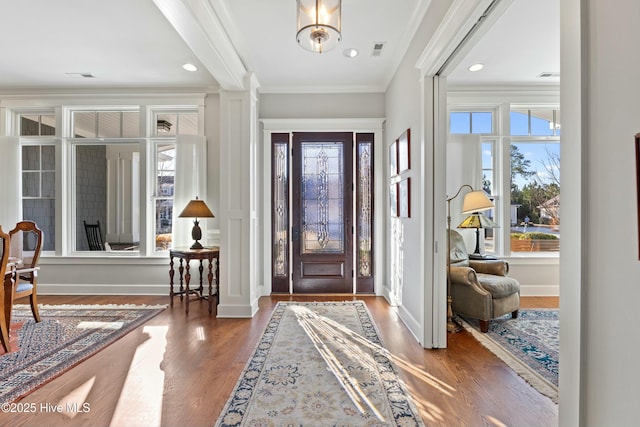 foyer entrance with visible vents, baseboards, wood finished floors, and ornamental molding