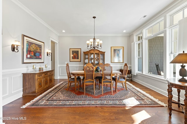 dining room with an inviting chandelier, ornamental molding, dark wood-style flooring, and a decorative wall