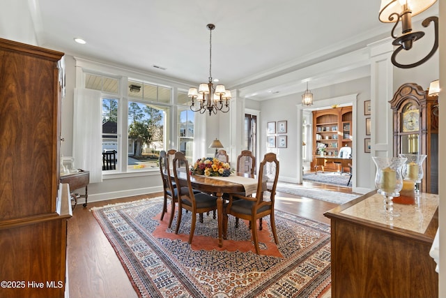 dining space featuring wood finished floors, visible vents, baseboards, crown molding, and a chandelier