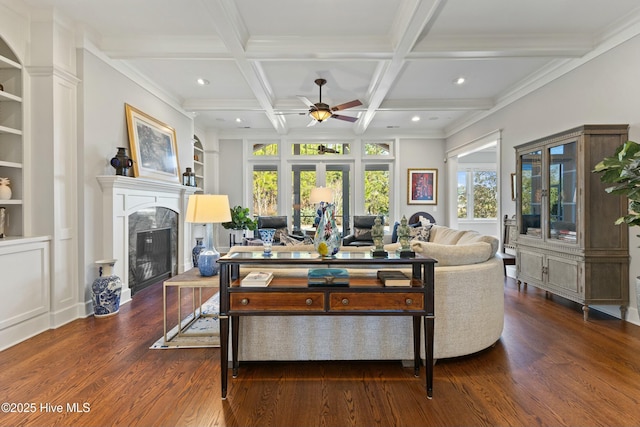 living area featuring beam ceiling, a ceiling fan, built in features, a high end fireplace, and dark wood-style flooring