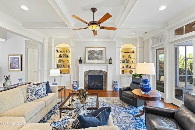 living area with built in shelves, beamed ceiling, a premium fireplace, wood finished floors, and coffered ceiling