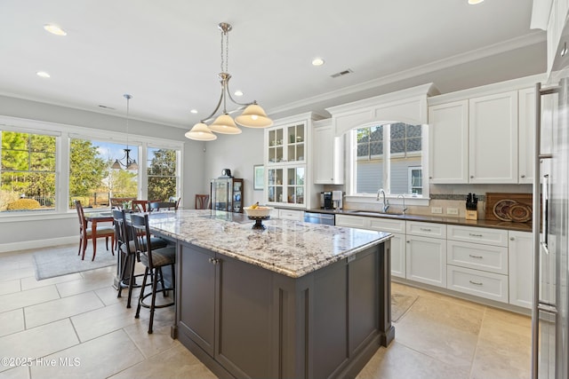 kitchen with a sink, visible vents, a kitchen island, and white cabinets