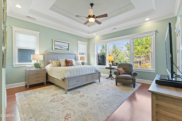 bedroom with visible vents, baseboards, a tray ceiling, and wood finished floors