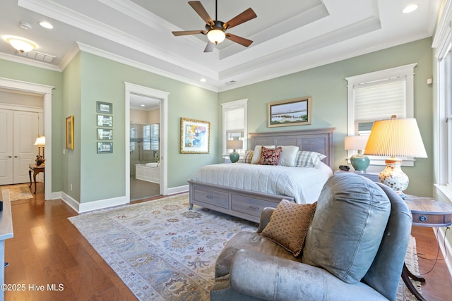 bedroom featuring ornamental molding, a tray ceiling, wood finished floors, connected bathroom, and baseboards