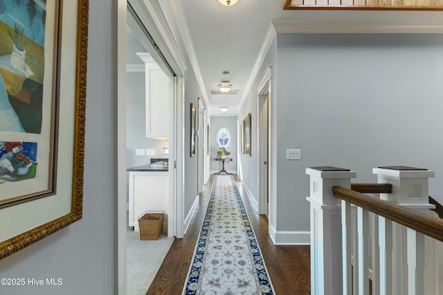 hall featuring baseboards, visible vents, dark wood-type flooring, crown molding, and an upstairs landing