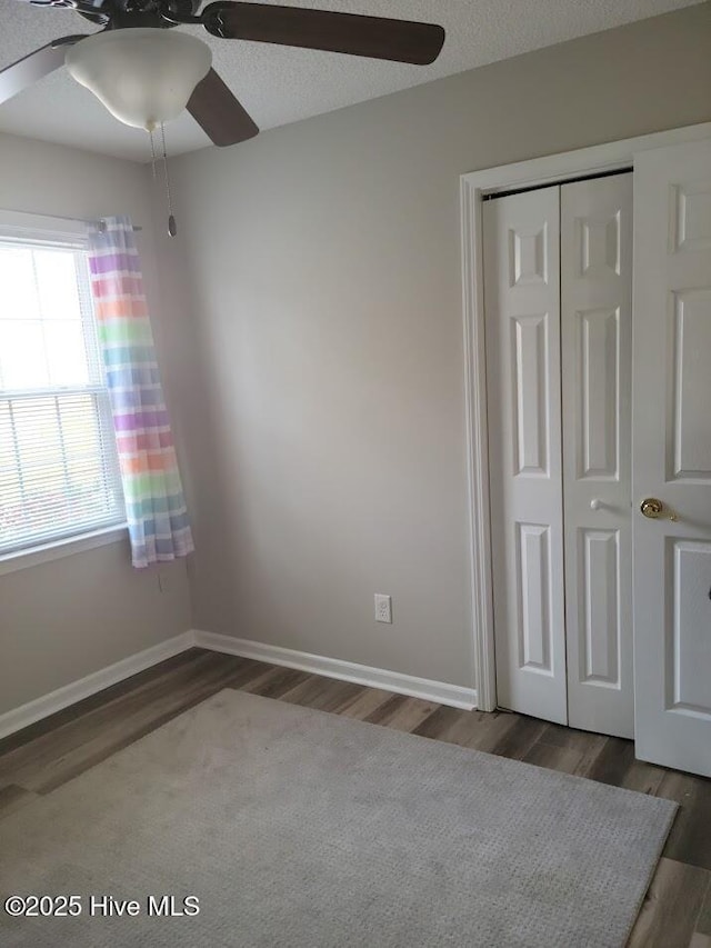 unfurnished bedroom featuring a textured ceiling, dark wood-type flooring, ceiling fan, and a closet