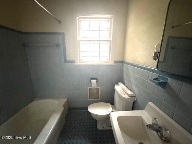 bathroom with toilet, sink, and tile walls