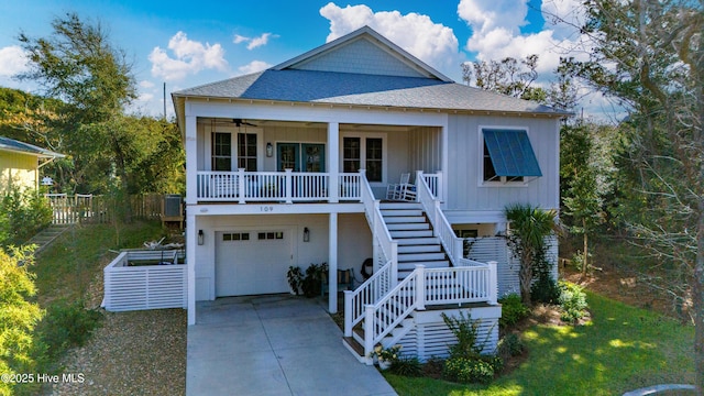 coastal home featuring a porch, a garage, a front yard, and ceiling fan