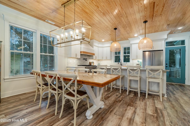 kitchen with a breakfast bar area, appliances with stainless steel finishes, white cabinetry, hanging light fixtures, and custom exhaust hood