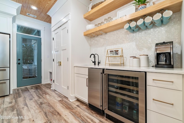 bar featuring sink, white cabinetry, tasteful backsplash, beverage cooler, and light wood-type flooring