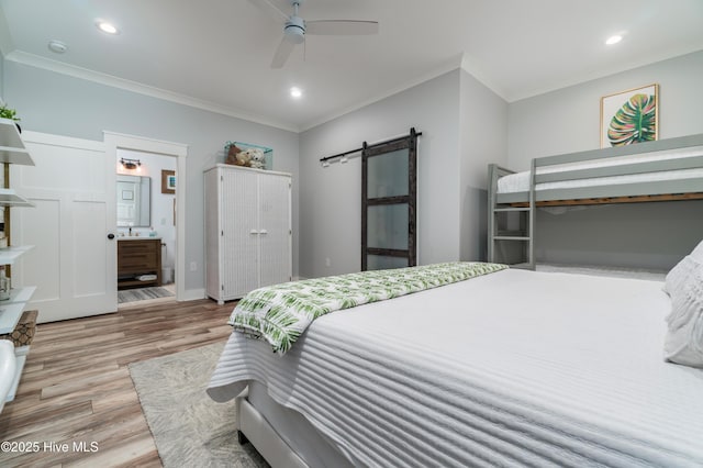 bedroom featuring connected bathroom, crown molding, a barn door, and light wood-type flooring