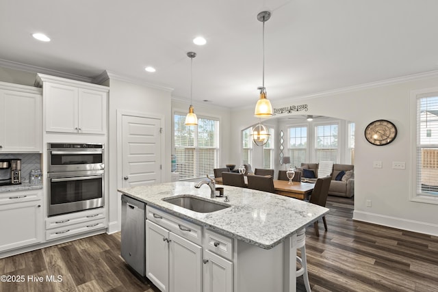 kitchen with sink, appliances with stainless steel finishes, white cabinetry, hanging light fixtures, and a center island with sink