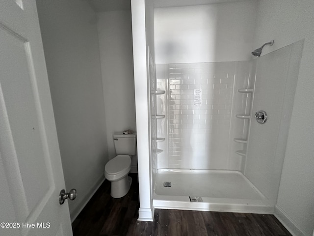 bathroom with baseboards, wood finished floors, toilet, and a shower stall