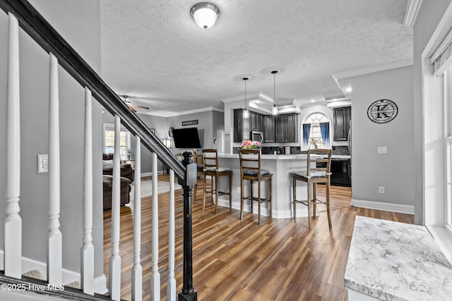 kitchen with a breakfast bar, decorative light fixtures, a textured ceiling, ornamental molding, and dark hardwood / wood-style floors