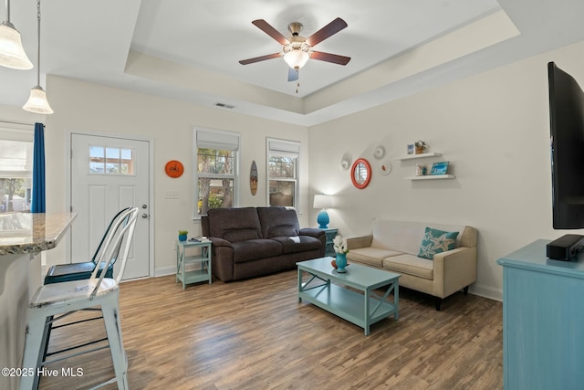 living area with baseboards, visible vents, a tray ceiling, and wood finished floors