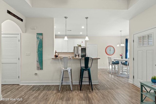 kitchen with baseboards, white cabinets, a breakfast bar area, wood finished floors, and stainless steel refrigerator with ice dispenser