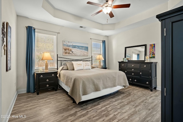 bedroom with ceiling fan, wood finished floors, visible vents, baseboards, and a tray ceiling