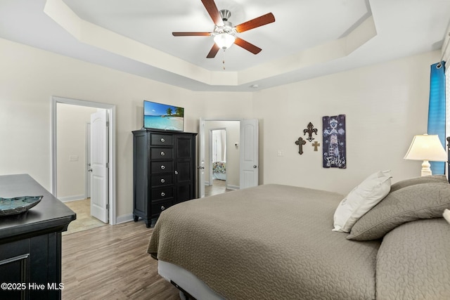 bedroom with light wood-type flooring, a raised ceiling, a ceiling fan, and baseboards