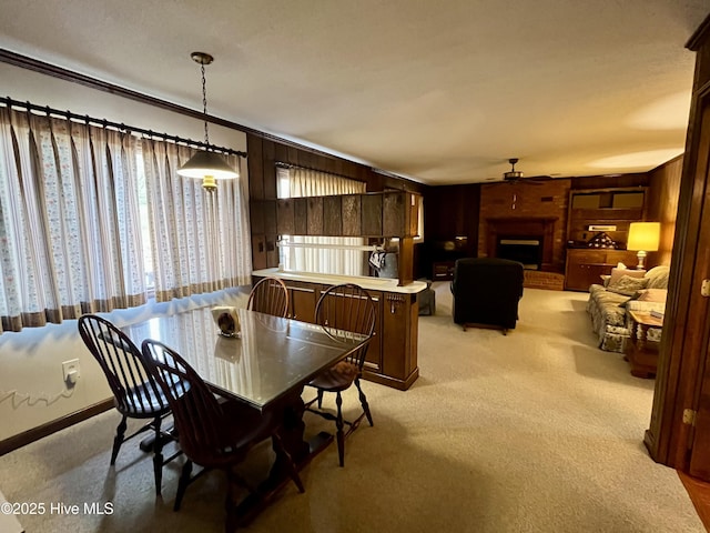 dining space with ceiling fan, light carpet, a brick fireplace, and wood walls