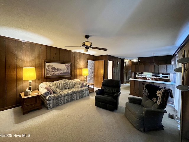 living room featuring ceiling fan, wooden walls, and light carpet