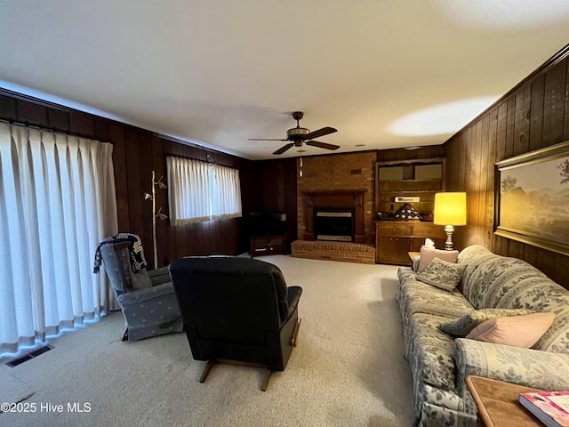 living room featuring a brick fireplace, wooden walls, light carpet, and ceiling fan