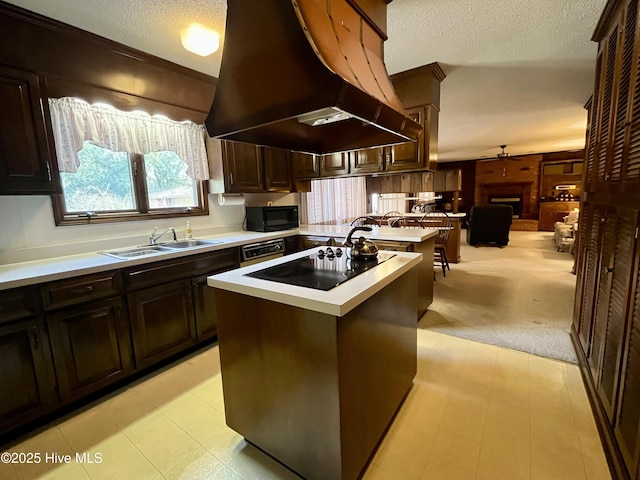 kitchen with sink, a center island, island range hood, black appliances, and a brick fireplace