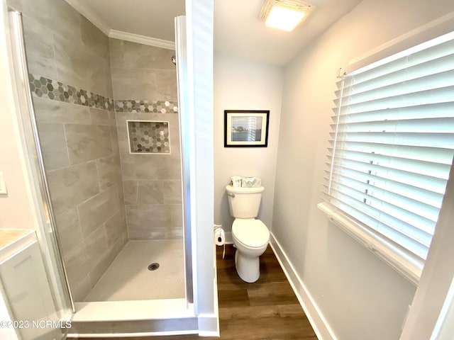 bathroom featuring hardwood / wood-style flooring, tiled shower, ornamental molding, and toilet