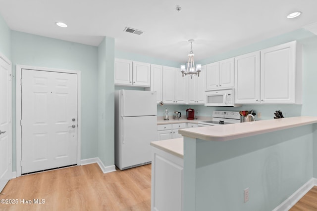 kitchen featuring white appliances, hanging light fixtures, and white cabinets