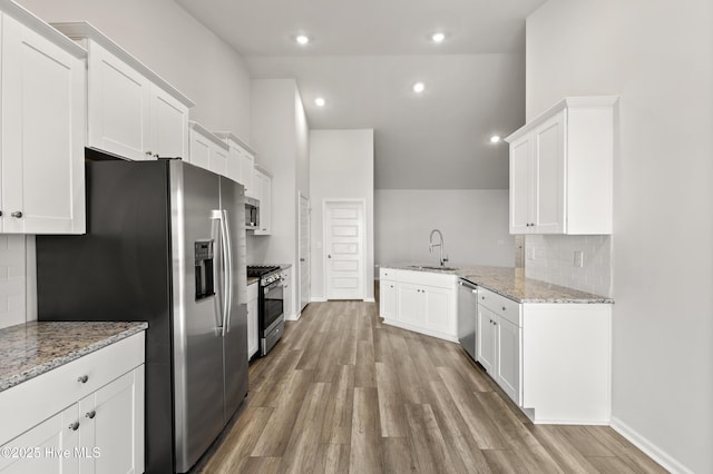 kitchen featuring light stone counters, appliances with stainless steel finishes, white cabinetry, and light wood-style floors