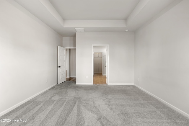 unfurnished bedroom featuring a spacious closet, carpet flooring, a raised ceiling, and baseboards