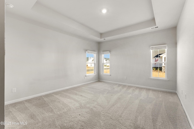 carpeted spare room featuring a raised ceiling, baseboards, and visible vents