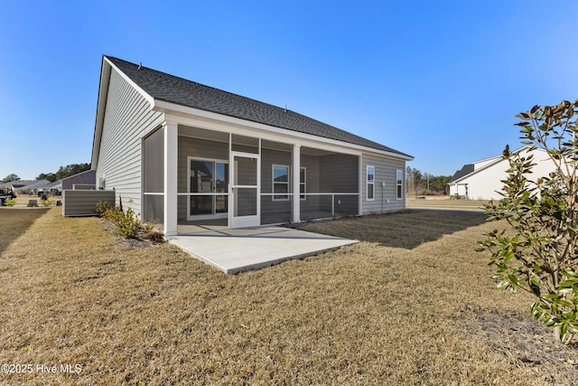 rear view of house featuring a patio, a lawn, a shingled roof, and a sunroom