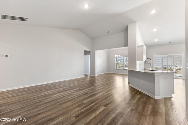 unfurnished living room featuring visible vents, dark wood-type flooring, vaulted ceiling, a notable chandelier, and a sink