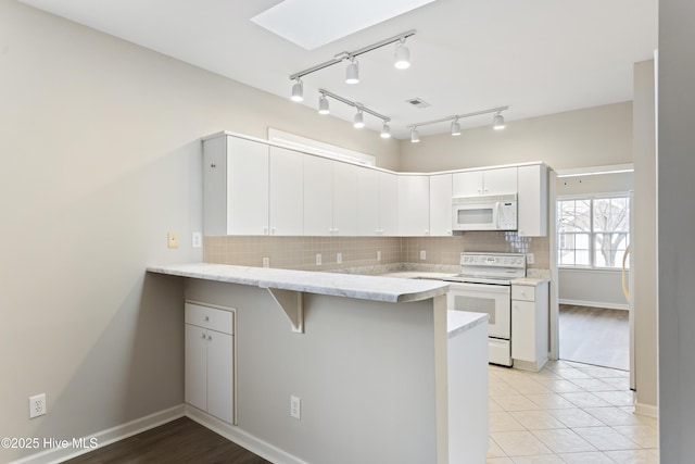 kitchen with white appliances, a peninsula, a skylight, a breakfast bar area, and decorative backsplash