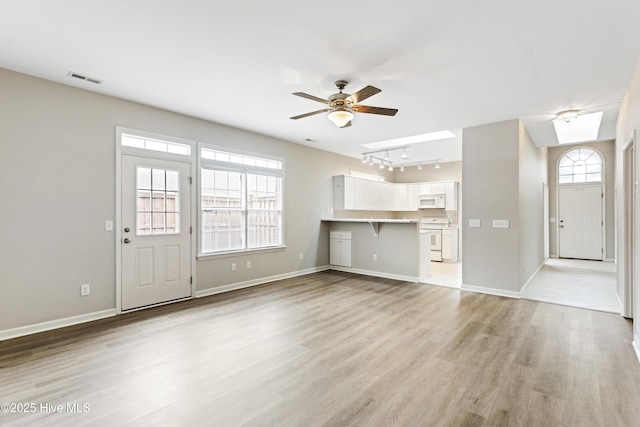unfurnished living room featuring rail lighting, a ceiling fan, light wood-type flooring, and baseboards