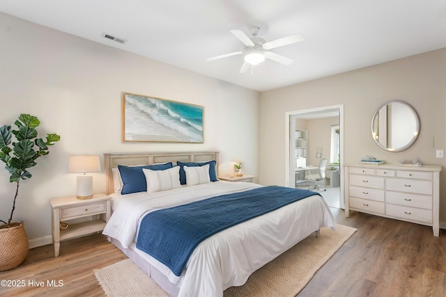 bedroom with wood finished floors, baseboards, a ceiling fan, and ensuite bath