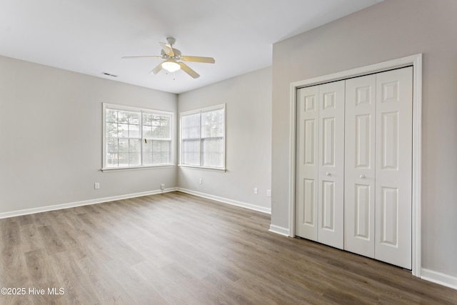 unfurnished bedroom with wood finished floors, a closet, baseboards, and a ceiling fan
