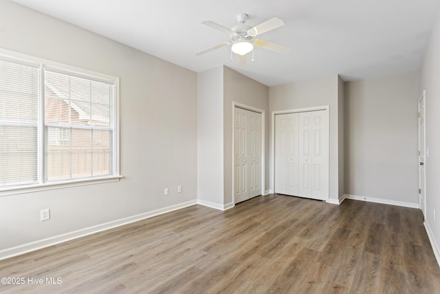 unfurnished bedroom featuring wood finished floors, multiple closets, baseboards, and ceiling fan