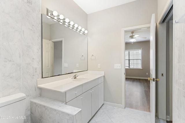bathroom with a ceiling fan, marble look tile flooring, toilet, vanity, and baseboards