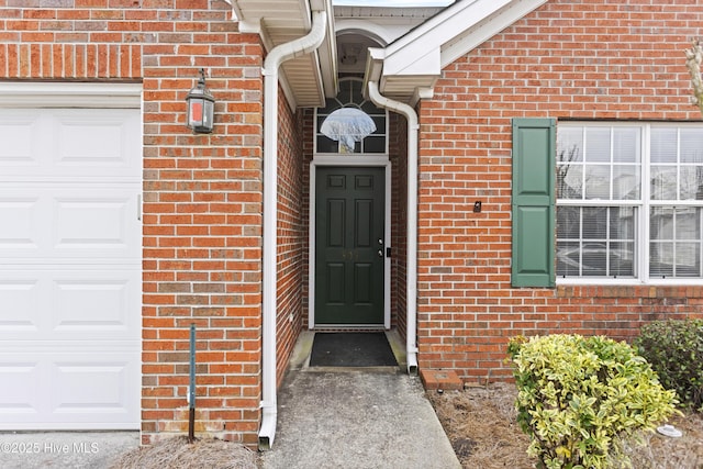 view of exterior entry featuring a garage and brick siding