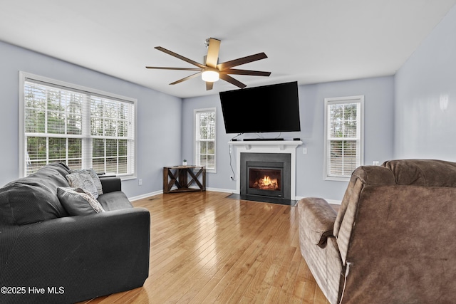 living room featuring a fireplace with flush hearth, plenty of natural light, light wood-type flooring, and baseboards