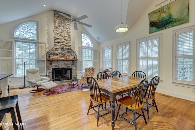 dining space with ceiling fan, a stone fireplace, high vaulted ceiling, and light wood-type flooring