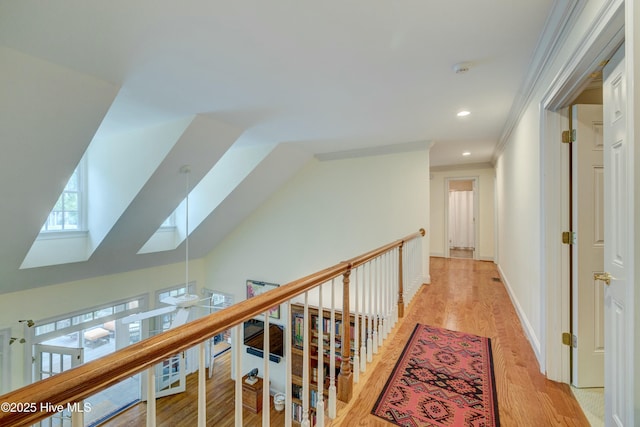 corridor with ornamental molding, lofted ceiling with skylight, and light hardwood / wood-style floors