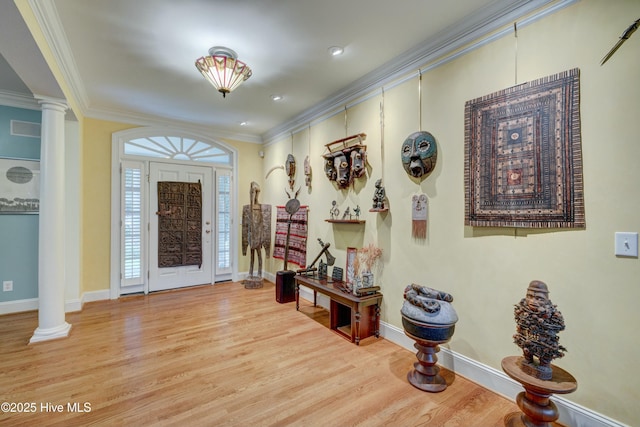 foyer entrance featuring decorative columns, crown molding, and light wood-type flooring