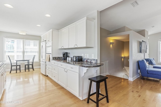 kitchen featuring visible vents, white cabinets, freestanding refrigerator, dark stone countertops, and a kitchen bar