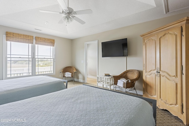 bedroom with a ceiling fan, baseboards, a tray ceiling, and a textured ceiling