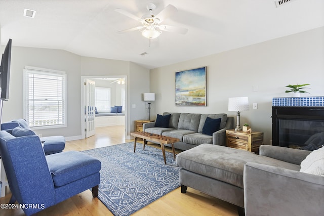 living room with visible vents, ceiling fan, light wood-style flooring, vaulted ceiling, and a fireplace