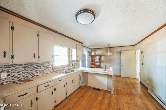 kitchen with sink, kitchen peninsula, pendant lighting, light hardwood / wood-style floors, and a baseboard heating unit