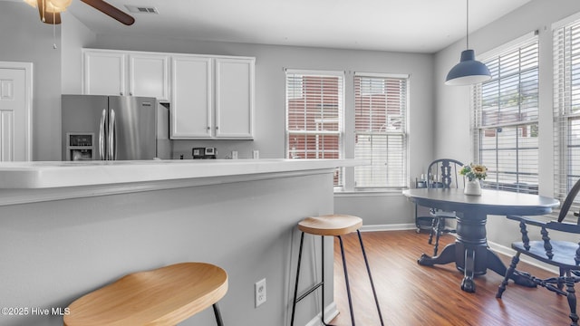 kitchen with decorative light fixtures, stainless steel fridge with ice dispenser, ceiling fan, hardwood / wood-style floors, and white cabinets