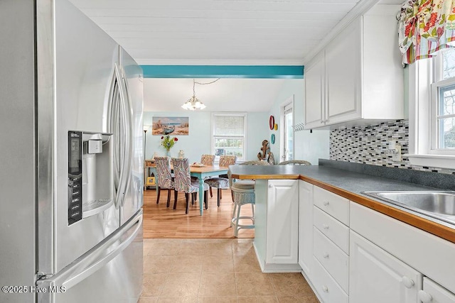 kitchen with stainless steel fridge, hanging light fixtures, backsplash, plenty of natural light, and white cabinets